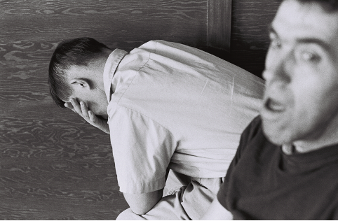 A black and white photograph of two Mansfield Training School residents. One sits near the camera with his mouth open and the other sits in the backdrop with his face in his hands.