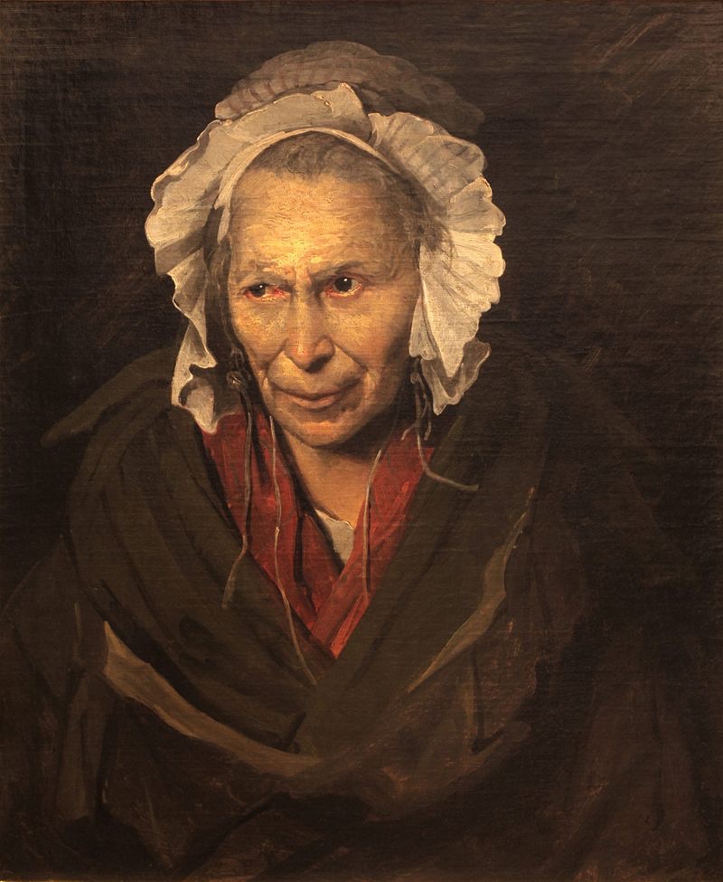 Portrait of an older woman wearing a white bonnet and dark shawl, looking directly toward the viewer with a slight smile. Her eyes and facial expression are clearly visible.
